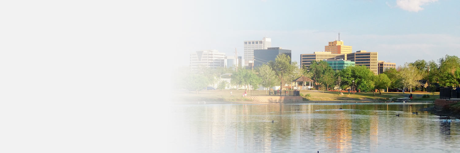 A view of Odessa, TX with buildings in the background and a park with a pond with ducks in it