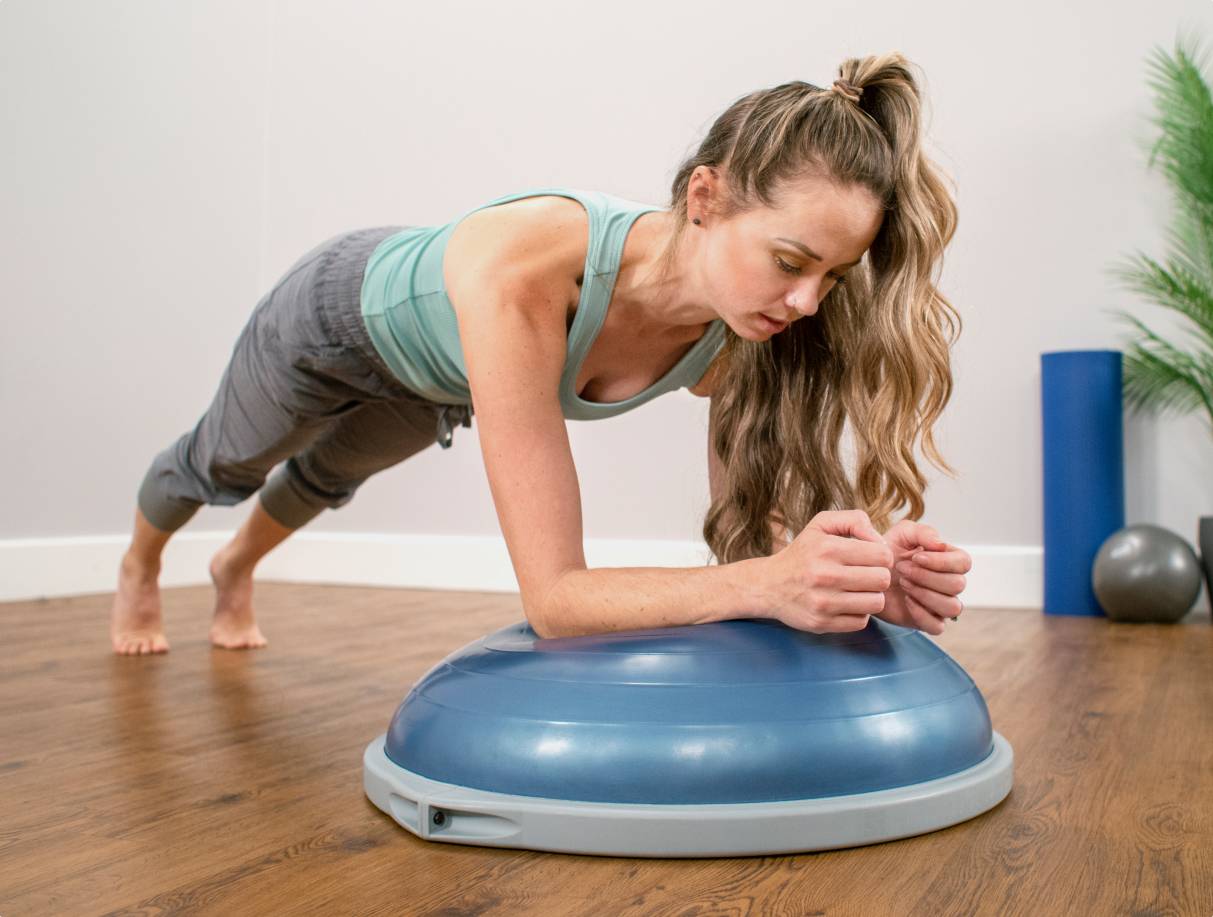 woman in plank position with her elbows resting on a bosu