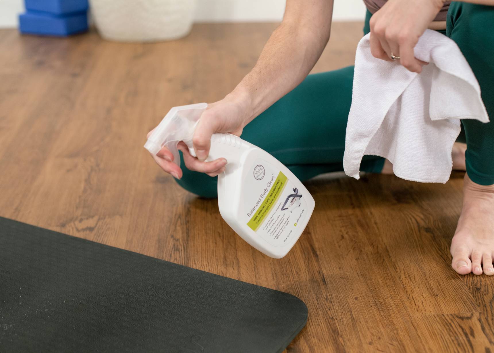 Person spraying Balanced Body Clean on a mat for hygiene.