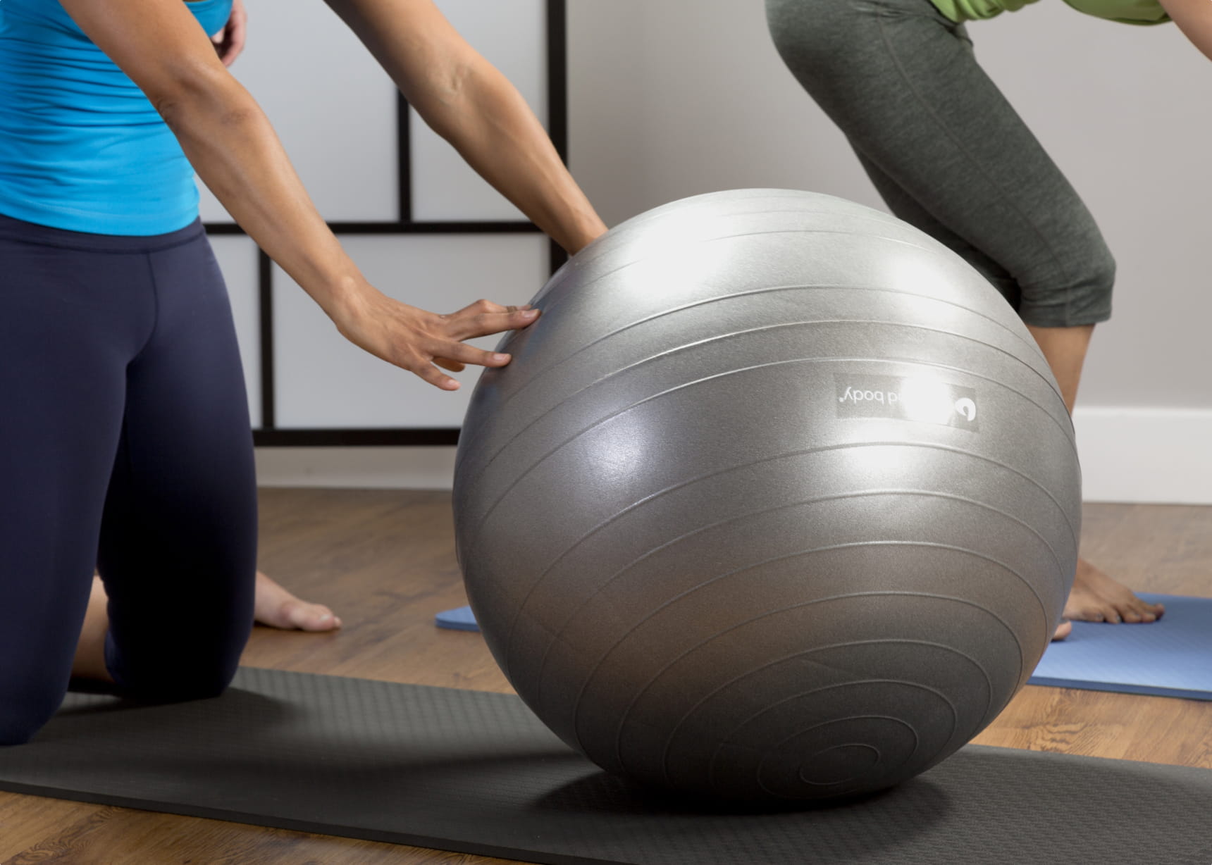 teenager kneeling out of frame leaning in with hands on a large gray fitness ball during a Pilates class