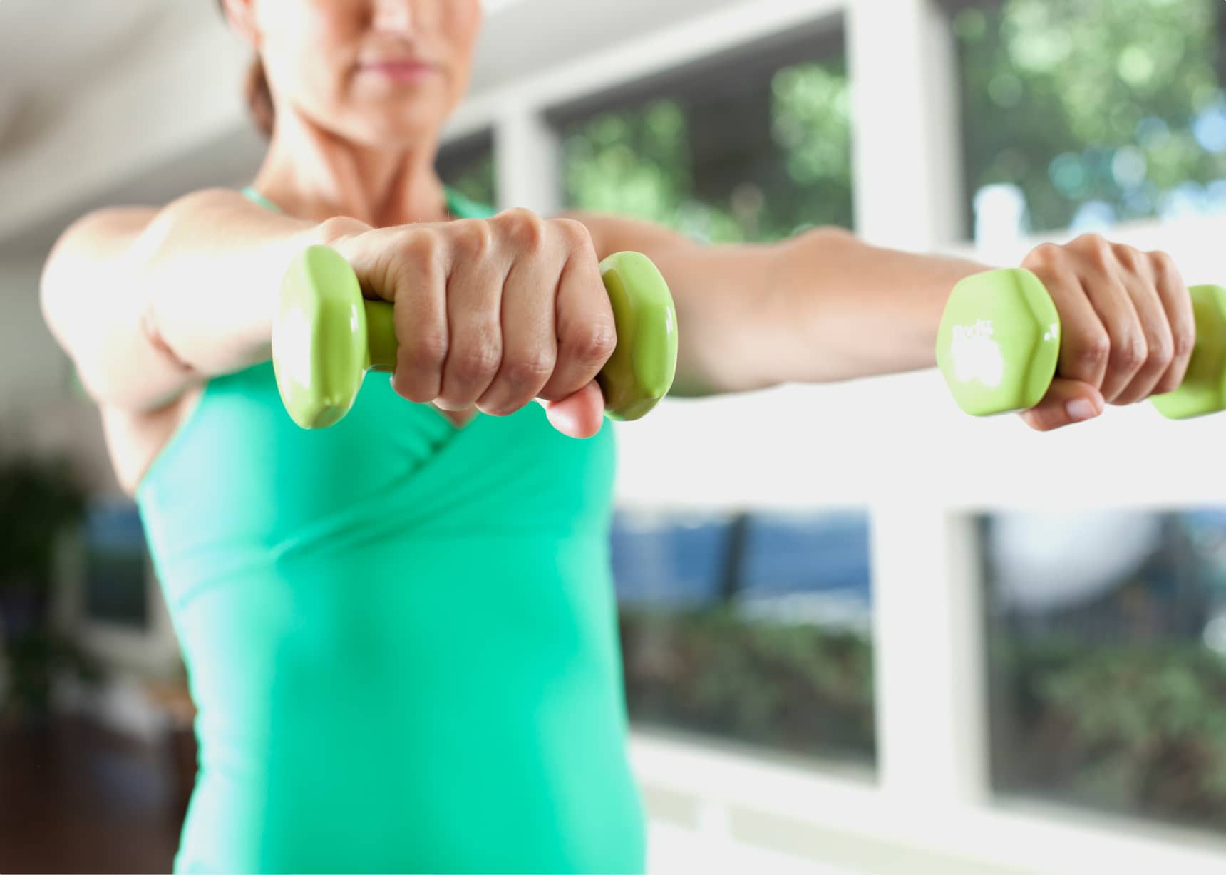 closeup of womans arms outstretched with hands gripping green hand weights