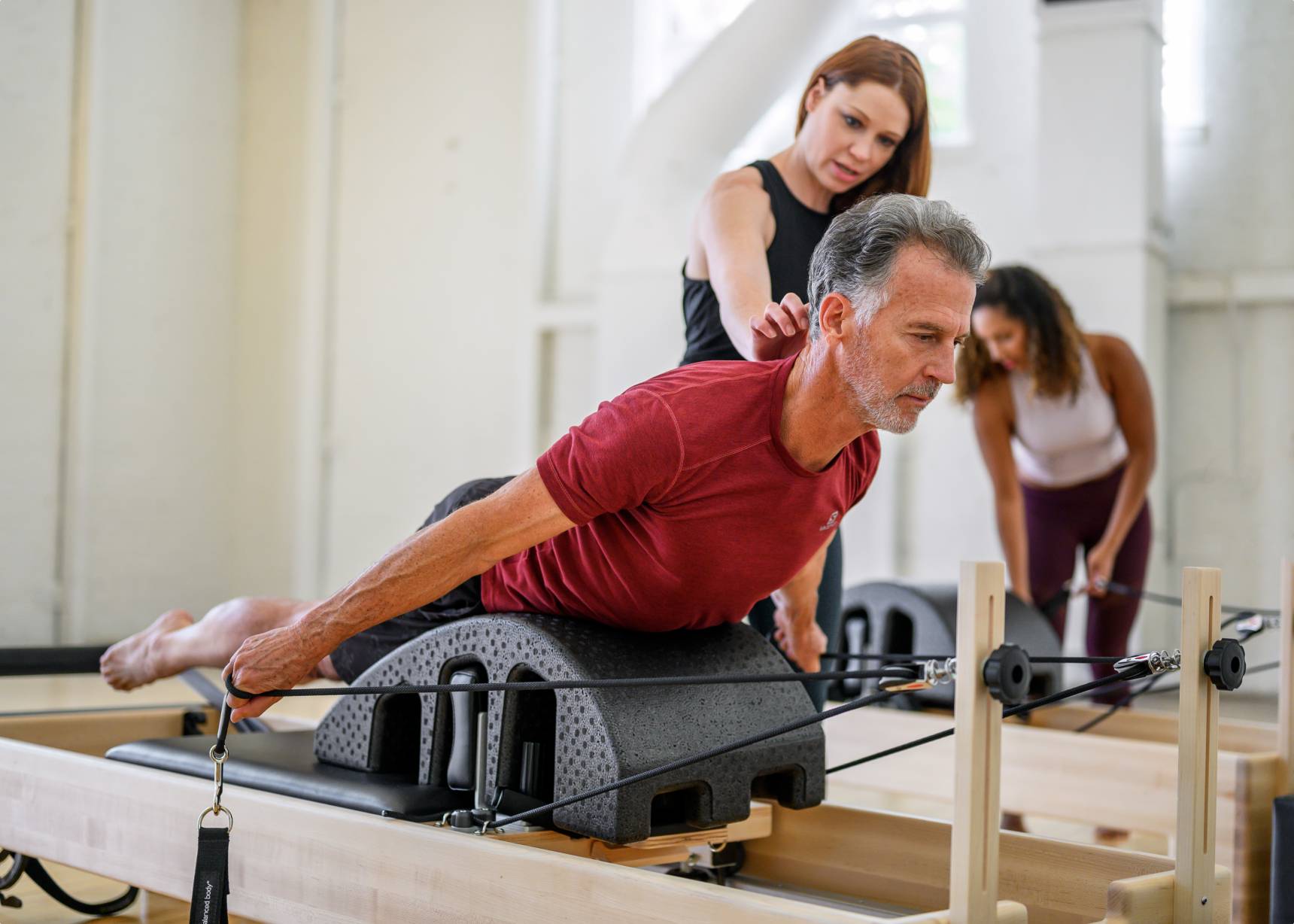 A man engaging in a workout on a Pilates reformer under the guidance of an instructor.