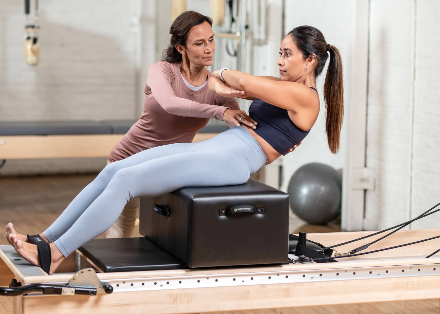 physical therapist helping patient strengthen their core with a sitting box on a Pilates Reformer