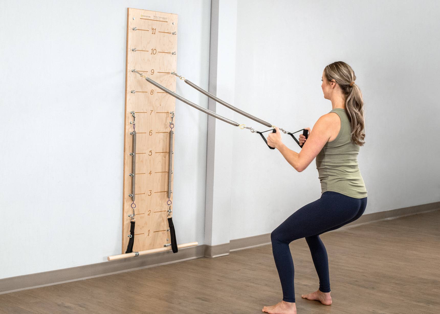 Woman pulling Pilates Springboard straps, which are affixed to a wall.