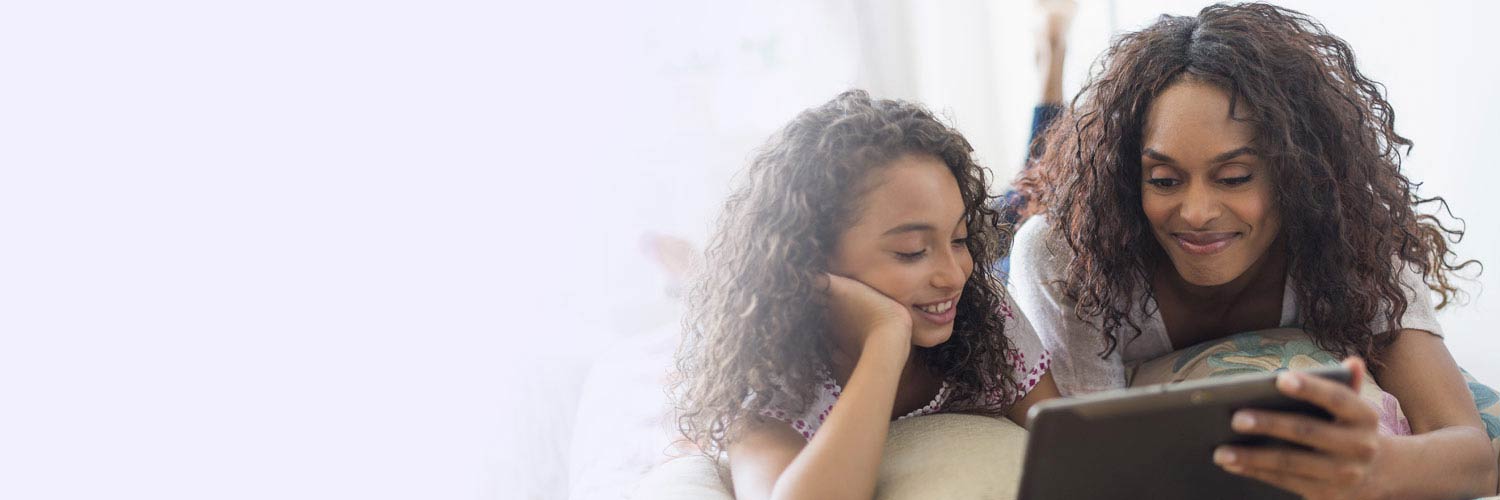 parent and child smiling while enjoying a movie on their tablet