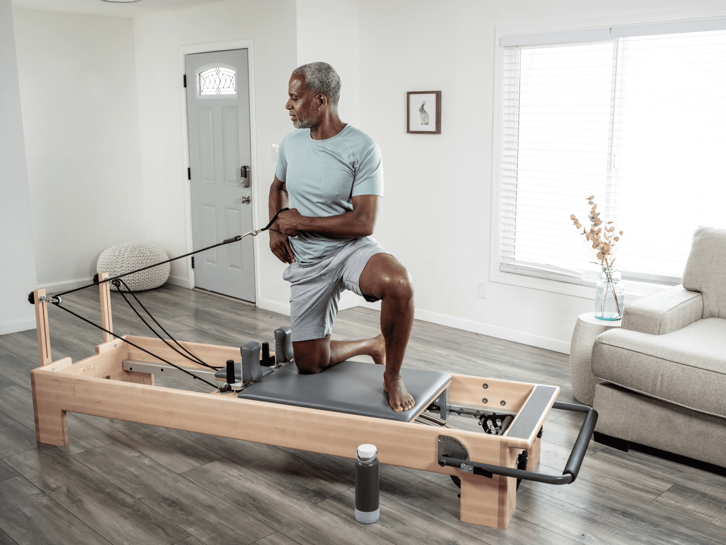 older man using balanced body reformer for pilates exercises at home