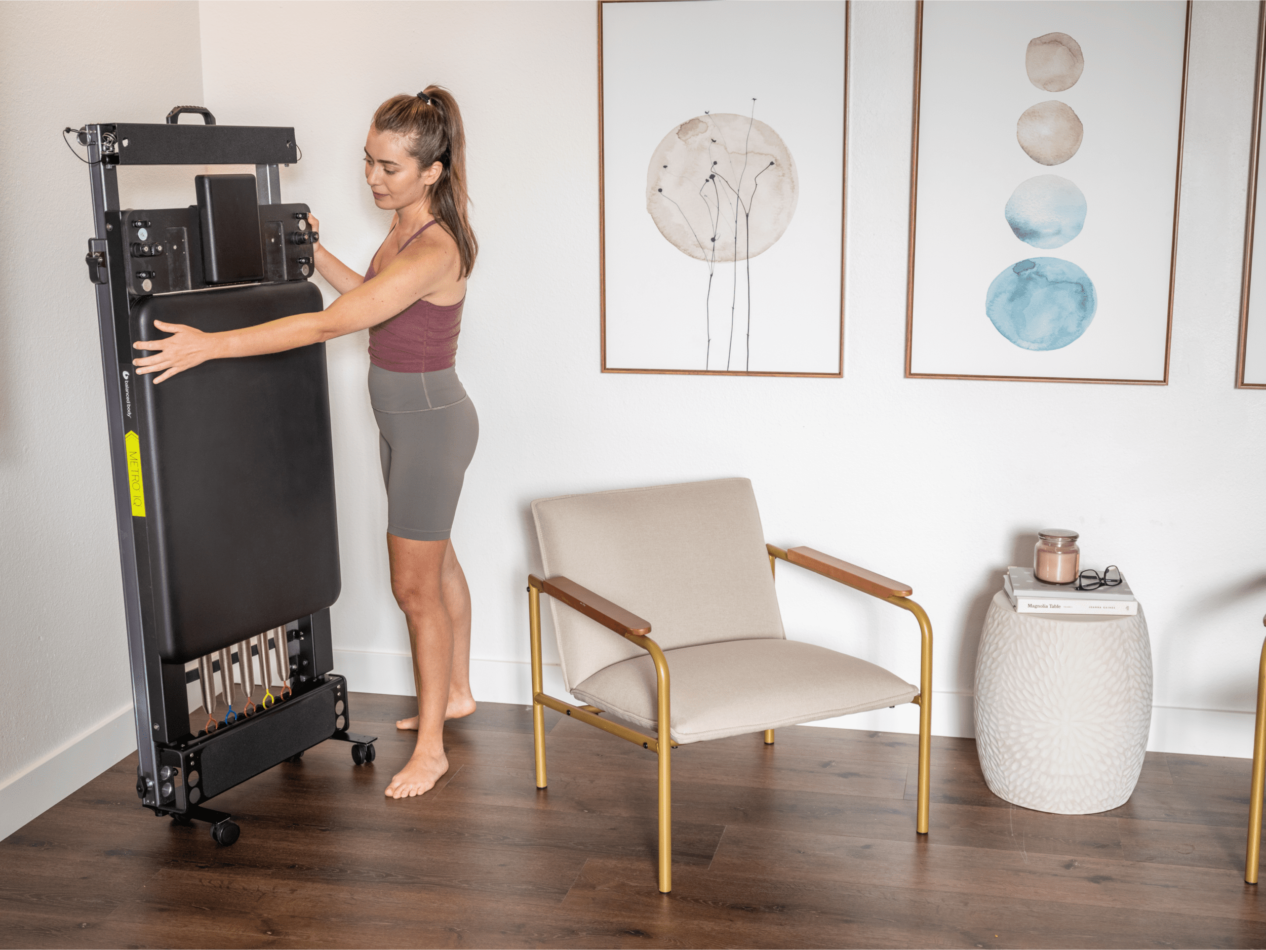 A woman is storing a Metro-IQ Pilates Reformer vertically on a wall.